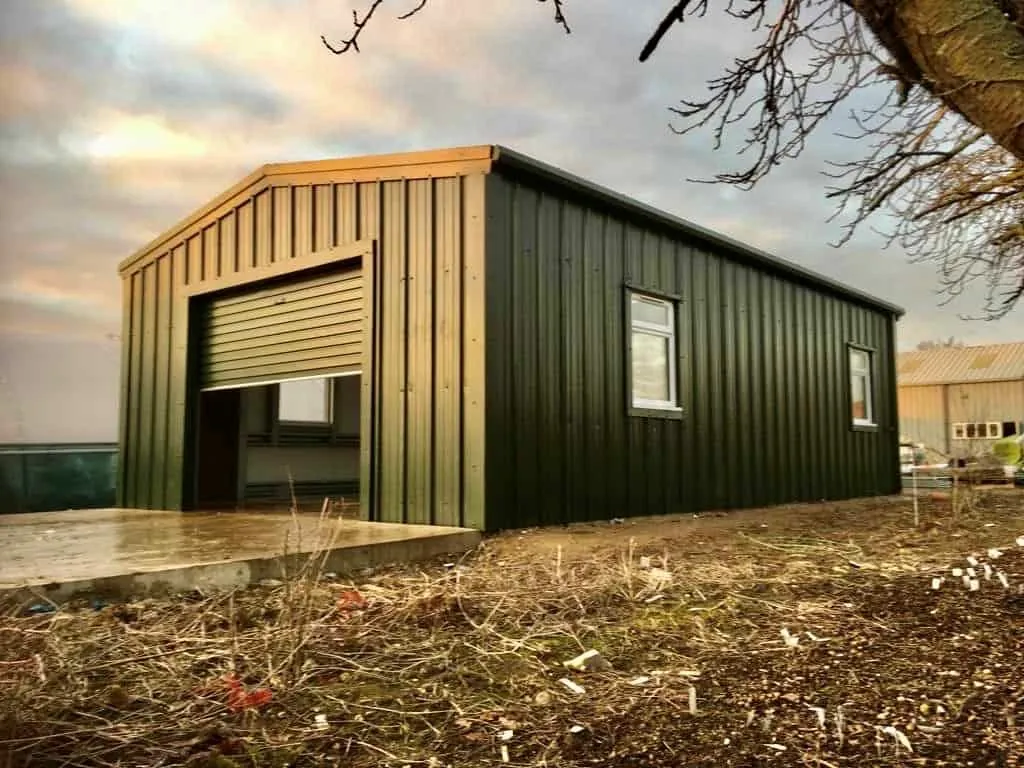 Cold rolled steel garage in dark green cladding with a roller door and side window